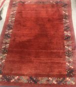 A Persian rug, the plain red ground set with a border of geometric blue and cream design approx.