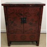 A Chinese red lacquered dwarf cabinet of two doors decorated with watery mountainous landscapes and