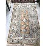 A Caucasian rug, the central panel set with five repeating medallions on a salmon pink ground,