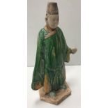 A Chinese terracotta man with green and yellow glazed robes set on a hexagaonal base in the