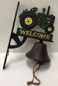 A modern cast metal and painted wall mounted bell with tractor decoration and inscribed "Welcome"