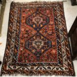 A Caucasian carpet, the central panel set with two repeating medallions on a blood red ground,