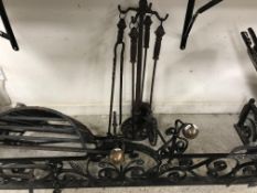 A wrought iron scrollwork decorated fire fender with central flower head medallion and ball end