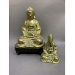 A brass figure of a Thai deity sat in lotus position on a hardwood stand together with another