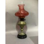 A Victorian brass and black glass base oil lamp stamped Messengers Patent with a cranberry glass