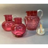 Three cranberry glass jugs with clear handles, one with dimpled body together with a Mary Gregory