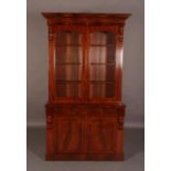 A VICTORIAN FIGURED MAHOGANY BOOKCASE CUPBOARD, having a moulded cornice above two arched glazed