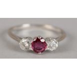 A RUBY AND DIAMOND THREE STONE RING, the oval faceted ruby claw set in line, flanked by two