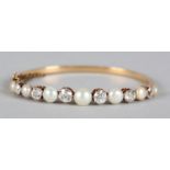 AN EDWARD VII PEARL AND DIAMOND STIFF HINGED BANGLE in 14ct gold, the graduated Old European cut