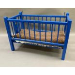 A blue painted doll's cot with railed sides, with transfer figures, 61cm long