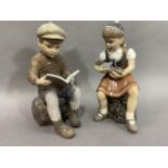 A pair of Royal Copenhagen figures of a boy reading a book sitting on a rock and a girl playing with