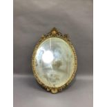 An oval wall mirror in gilt plaster frame with shell and leaf scroll pediment and apron