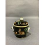 A small two handled jar and cover with fruit finial painted with rabbit, fruits and palm tree on a
