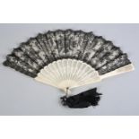 A 19th century black lace fan, the floral design offset by an underlayer of cream silk, the