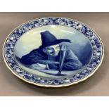 A Delft ware blue and white charger painted with a man contemplating a large flute of wine, after