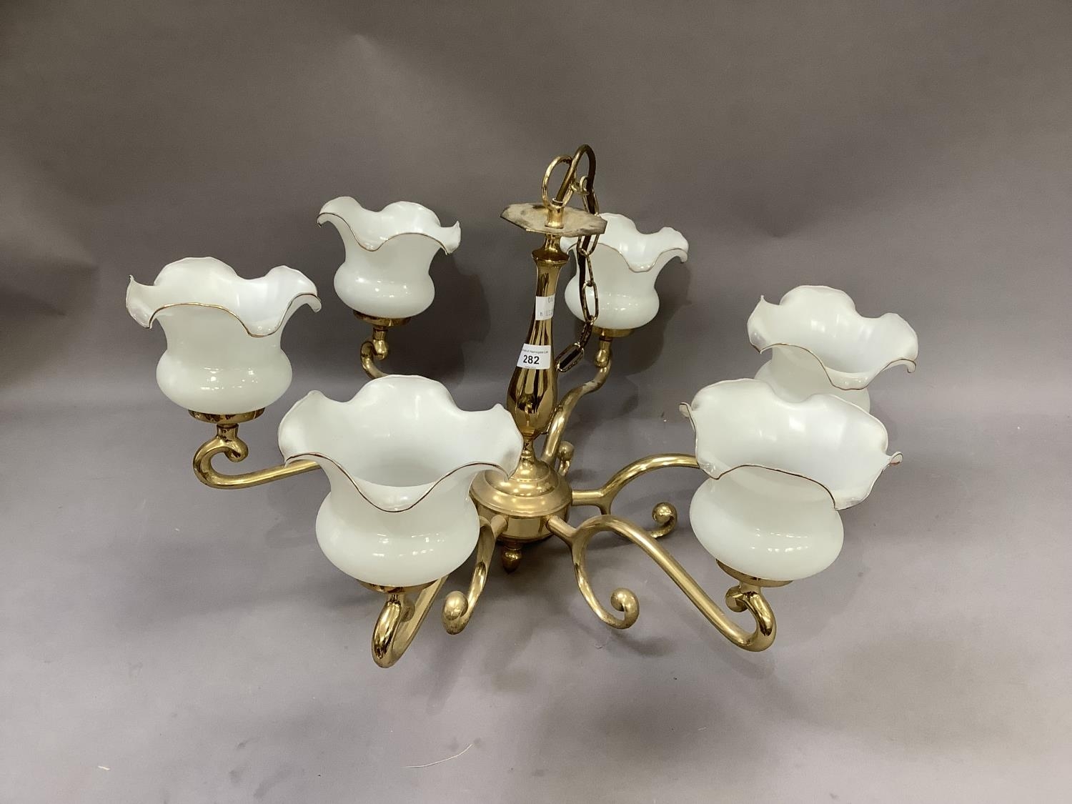 A brass six light chandelier with six white glass shades