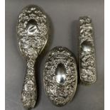 A silver backed hair brush and pair of clothes brushes of embossed mask and foliate design,