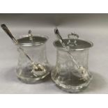A pair of George V silver lidded and glass preserve pots decorated with ribbon tied laurel wreaths
