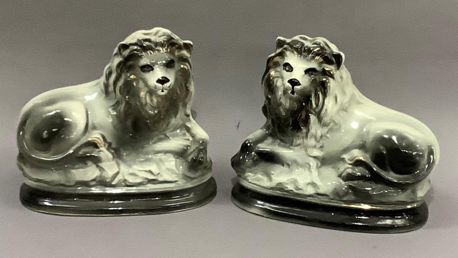 A pair of pottery lions, sponged in dark grey and highlighted in gilt