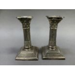 A pair of Edward VII silver Corinthian column candlesticks on square beaded and stepped bases,