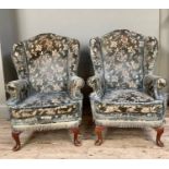 A pair of winged armchairs having an arched back, cut away arms and on oak cabriole legs with