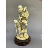 A Japanese ivory carving of a fisherman and his son carrying a toy boat and a rake, a fish at his