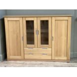 A four door beech cabinet having two glazed doors and glass shelves to the centre flanked by a