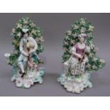 A pair of Derby porcelain seated bocage figures of a piper and hound and shepherdess with lamb,