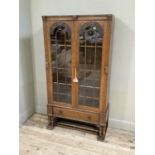 A 1930s oak and glazed two door bookcase, the arched glazing headed with foliate scroll carved