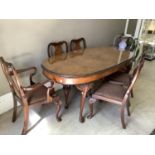 A figured walnut quarter veneered dining table with leaf carved rim, plate glass top and on cabriole