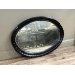An ebonised framed oval framed wall mirror with wavy frame, 106cm wide by 72cm high