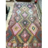 A large kelim rug of three rows of hooked diamond medallions in shades of pink, yellow, green, fox