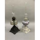 A pair of late Victorian cast iron oil lamps, the first of black metal work with clear glass