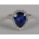 A SAPPHIRE AND DIAMOND CLUSTER in 18ct white gold, claw set to the centre with a pear shaped faceted