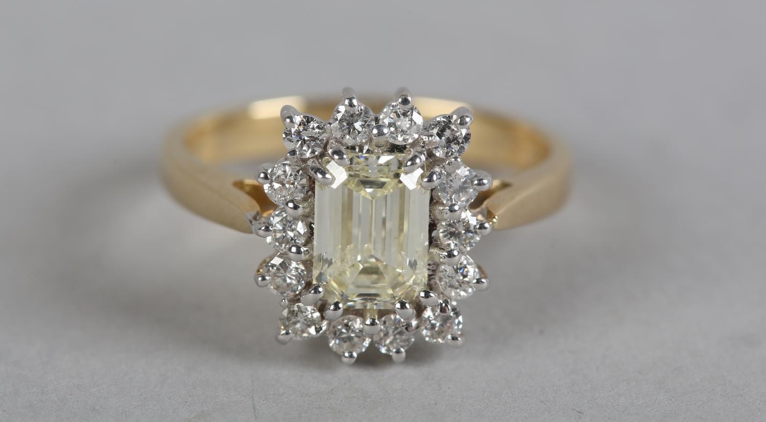 A DIAMOND CLUSTER RING in 18ct yellow and white gold, the step cut stone claw set to the centre