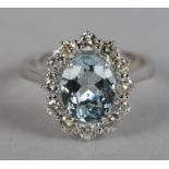 AN AQUAMARINE AND DIAMOND CLUSTER RING in 18ct white gold, the oval faceted aquamarine claw set to