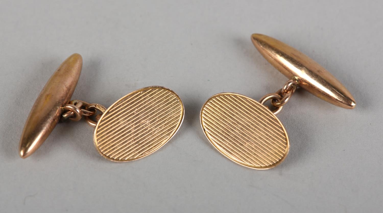 A PAIR OF GEORGE V CUFFLINKS BY G.H. JOHNSTONE & CO. in 9ct rose gold, the oval engine turned