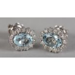A PAIR OF AQUAMARINE AND DIAMOND CLUSTER EAR STUDS, each claw set to the centre with an oval faceted
