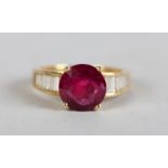 A RUBY AND DIAMOND CLUSTER RING, the circular faceted ruby claw set raised against channel-set