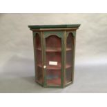 A green painted hanging corner cupboard with glazed door and glazed side panels