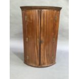 An early 19th century mahogany bow fronted hanging corner cupboard, three shelves and small