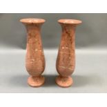 A pair of coral coloured marble vases of slender baluster form on circular foot, 30cm high