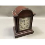 An Edwardian mahogany mantel clock of domed architectural form, the silvered dial with black Roman