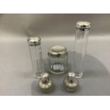 A pair of silver lidded glass salts bottles together with two silver lidded cylindrical and panelled