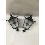 A pair of black wrought iron lanterns with scroll pediment and frame, two panes of glass missing