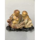 A carved soapstone figure group of a female offering peaches to a corpulent figure on hardwood