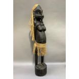 A carved African fertility figure of a female with string hair and skirt, standing on an oval