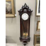 A dark mahogany wall clock with enamelled two part dial, exposed pendulum, glazed case with