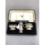 A George V silver three piece condiment set with blue glass liners, of circular outline with pierced