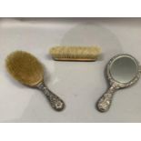Three silver backed dressing table items of embossed rocaille decoration comprising hand mirror,